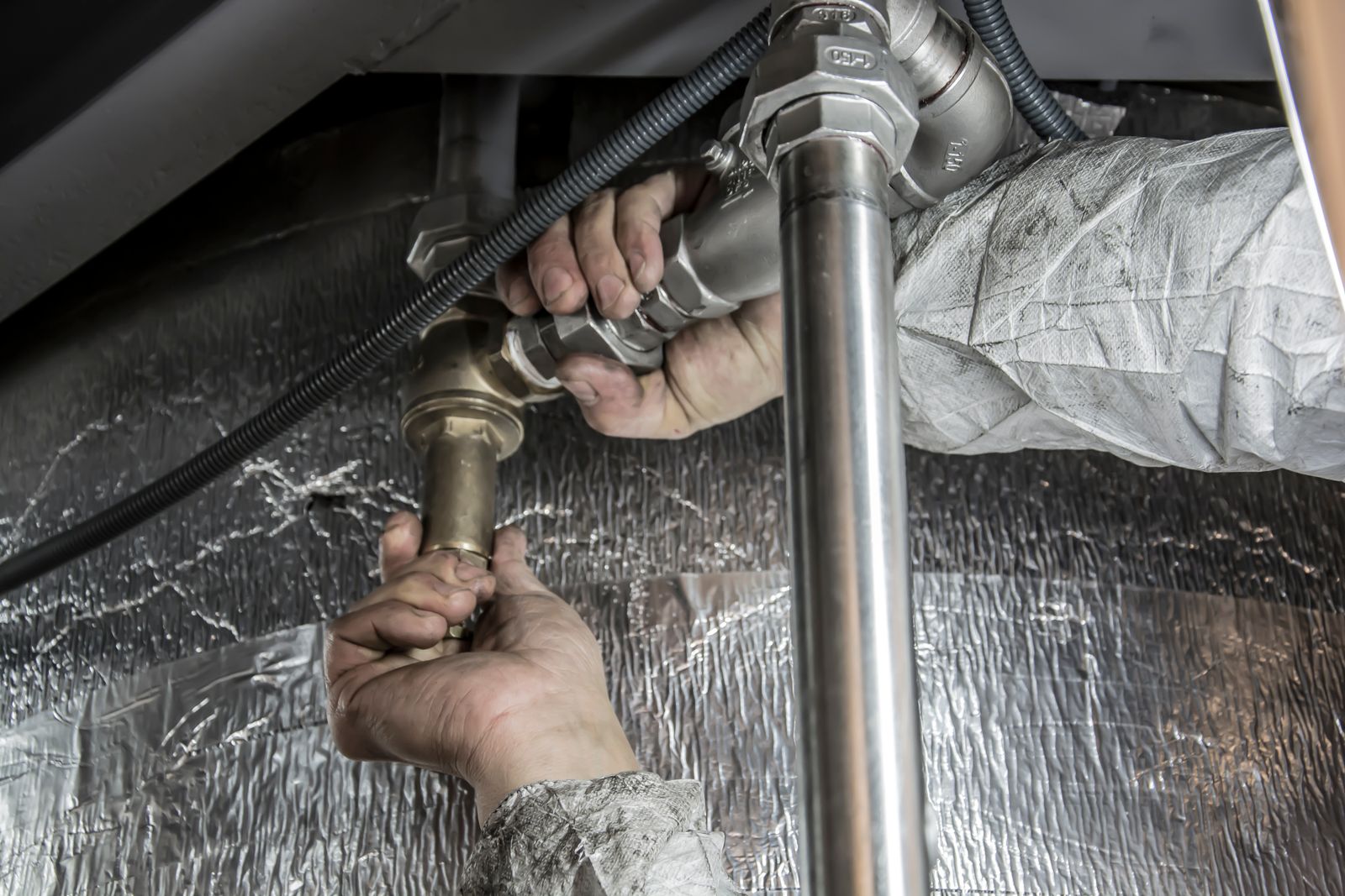 Plumber's hands fitting a water pipe with tools